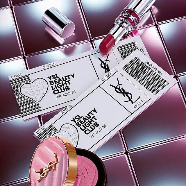 YSL Beauty products (lipstick and blush) arranged with ticket-style VIP access cards on a reflective metallic surface.