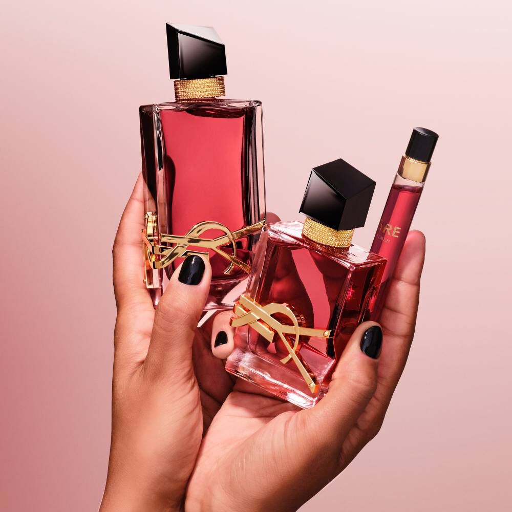 Hands with black nail polish holding three different sizes of YSL Libre fragrance bottles against a pink background.