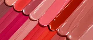 A close-up of various swatches of nail polish in a range of pink, nude, and coral shades, arranged in a gradient.