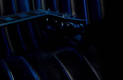 A close-up view of a sleek electric guitar resting on a dark textured surface, with a stylish fragrance bottle placed at an angle on the guitar. The overall color scheme features deep blues and blacks, creating an elegant atmosphere.