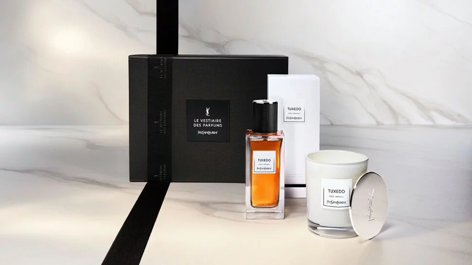 A stylish gift set featuring a bottle of perfume and a scented candle, elegantly presented in a black box with a sleek design on a marble surface.