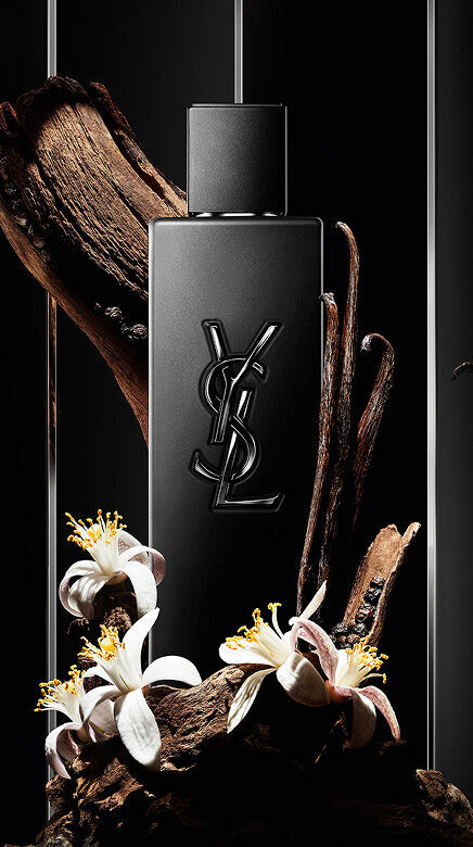 Black YSL perfume bottle surrounded by wood, vanilla pods, and white flowers.