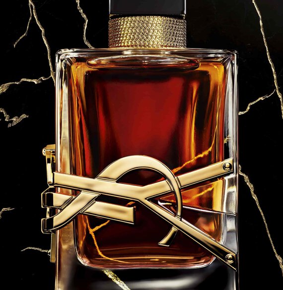 A close-up of a luxurious perfume bottle with a gold and black design, featuring a striking gold emblem and a dark, rich liquid inside, set against a dark, marbled background.