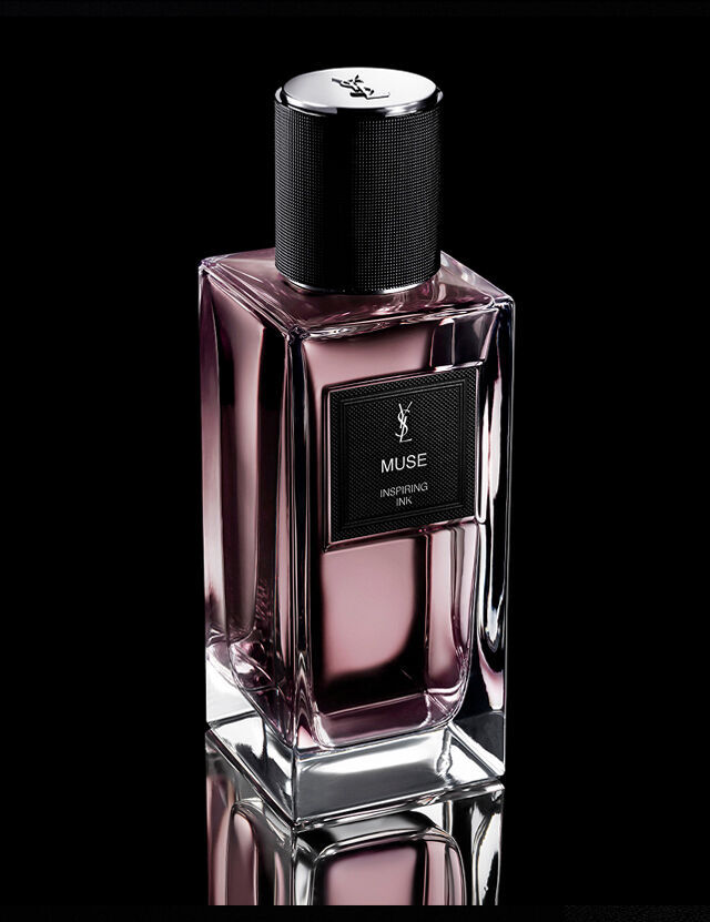 A rectangular, pink-tinted perfume bottle labeled "MUSE INSPIRING INK" by YSL, with a black textured cap, sits on a reflective surface against a dark background.