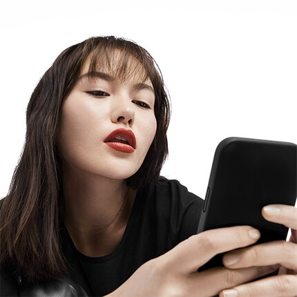 A close-up of a young woman with long dark hair and bold red lipstick, intently looking at a smartphone.