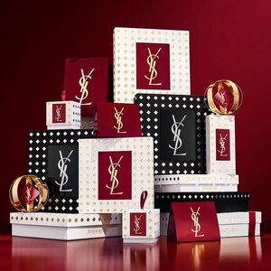 Yves Saint Laurent holiday collection gift sets and luxury beauty products displayed against a festive red background.