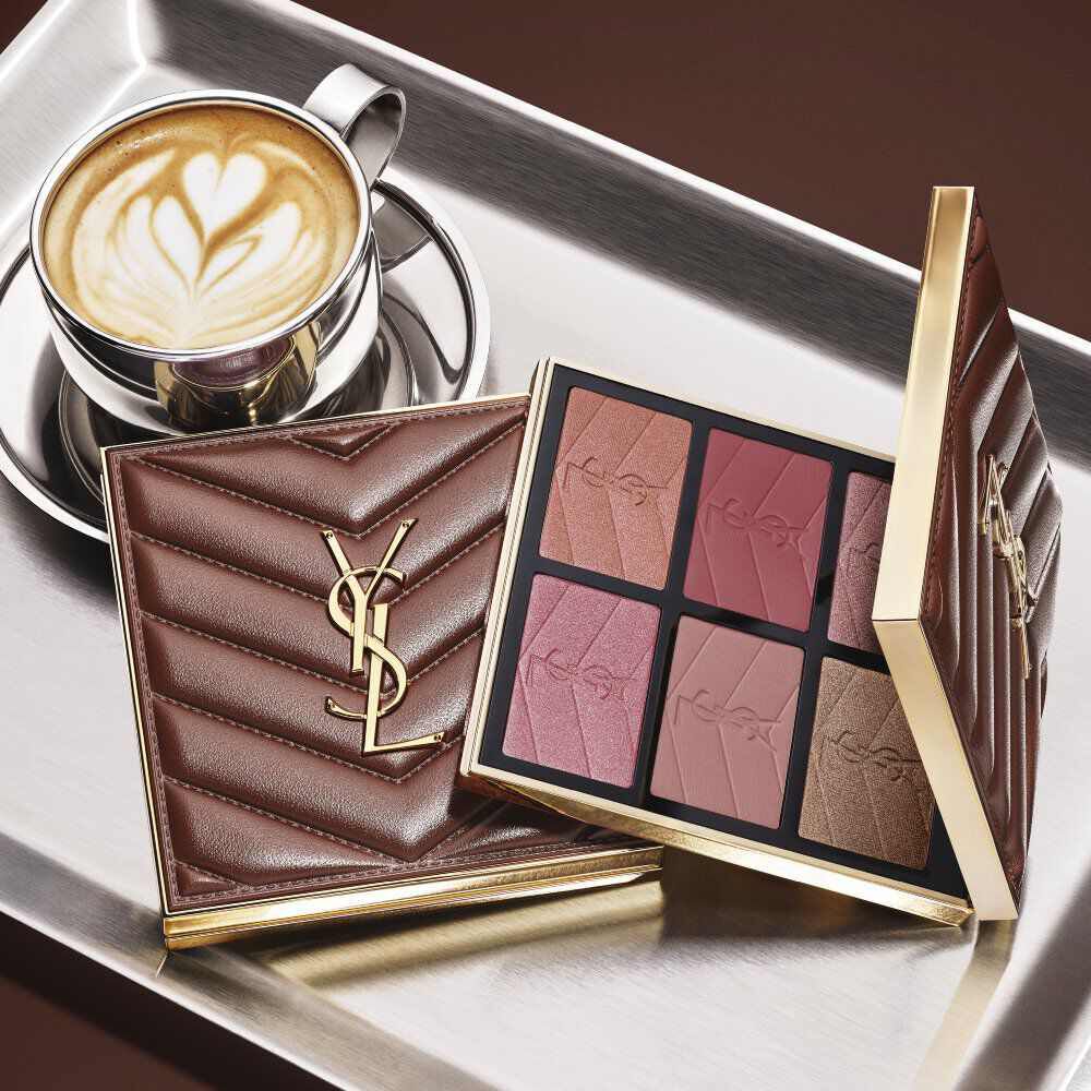 YSL makeup palette and quilted clutch beside a cup of coffee on a silver tray.