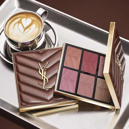 YSL makeup palette and quilted clutch beside a cup of coffee on a silver tray.
