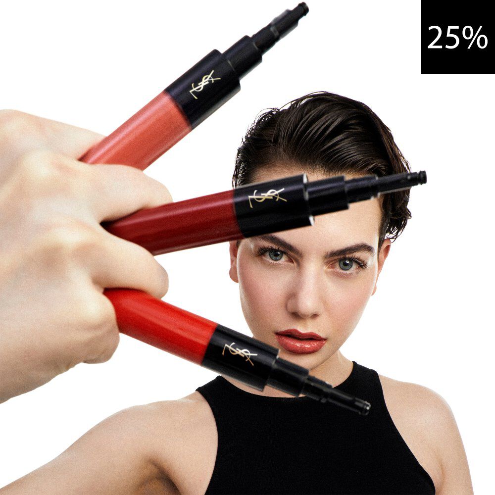 A close-up image featuring a model looking forward, with a hand holding three YSL liquid lip products in shades of red and coral. A black square with white text '25%' is visible in the top right corner, indicating a discount.