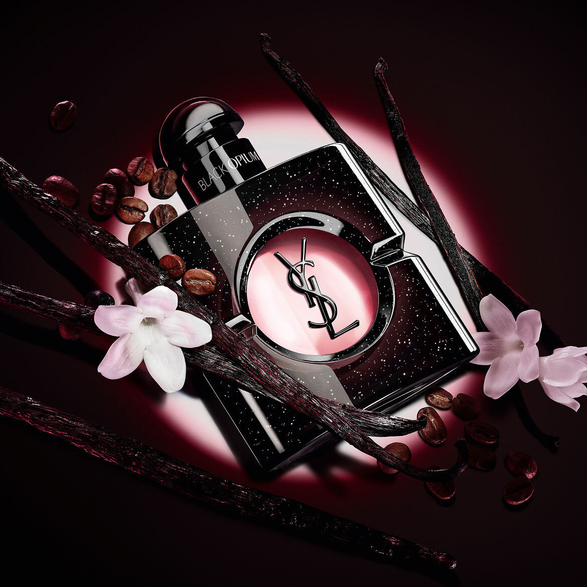 Black Opium Eau de Parfum bottle with white jasmine flowers, vanilla pods, and roasted coffee beans.