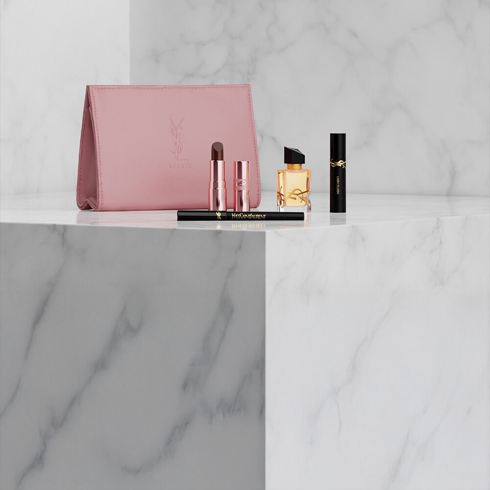 Pink YSL Beauty pouch with lipstick, eyeliner, perfume, and mascara on a marble shelf.
