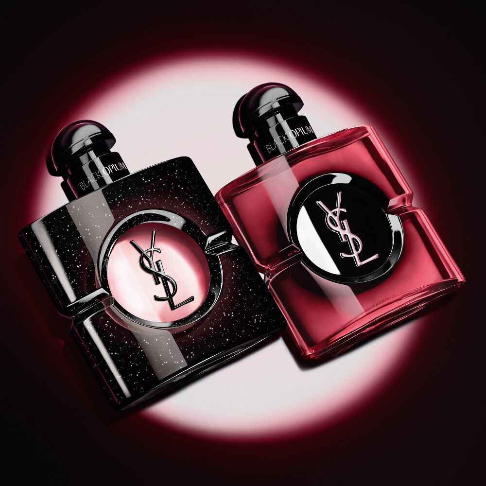 Two Yves Saint Laurent Black Opium perfume bottles illuminated on a dark background.