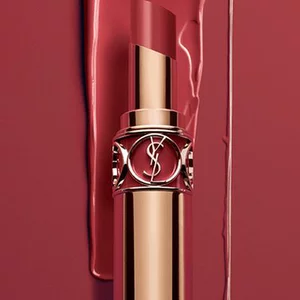 A close-up of a gold lipstick tube against a rich red background. The lipstick has an elegant design, emphasizing luxury and beauty.