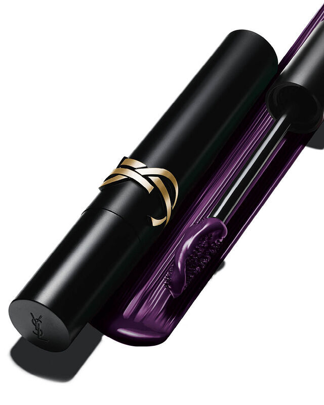 Close-up of a black mascara tube with a gold logo next to an open wand dipped in deep purple formula.