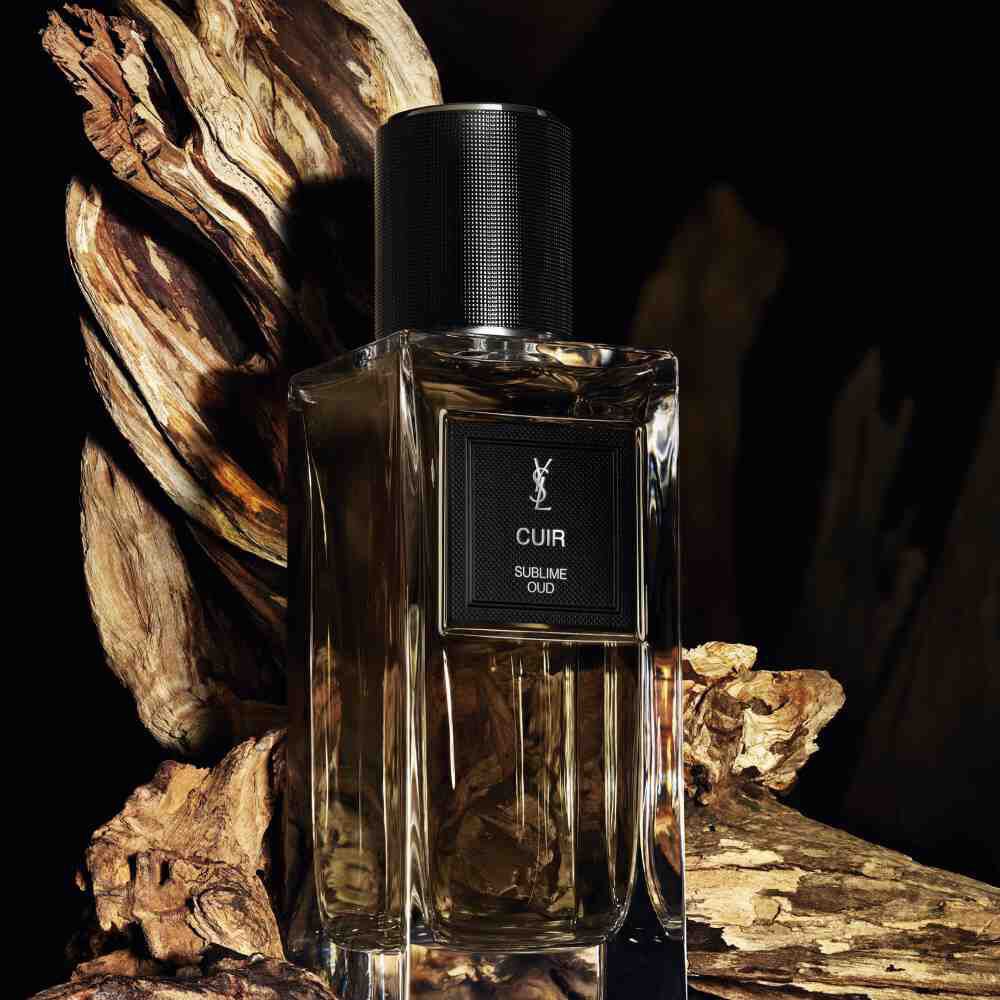 A brown-tinted perfume bottle labeled "CUIR SUBLIME OUD" by YSL, surrounded by pieces of aged, textured wood.