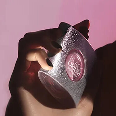 Woman holding a perfume bottle against a pink background
