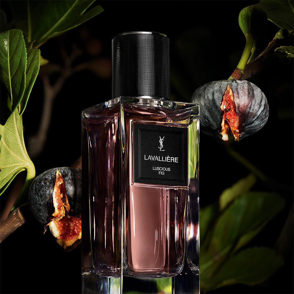 A purple-tinted perfume bottle labeled "LAVALLIERE LUSCIOUS FIG" by YSL, with fig branches and ripe, split figs.