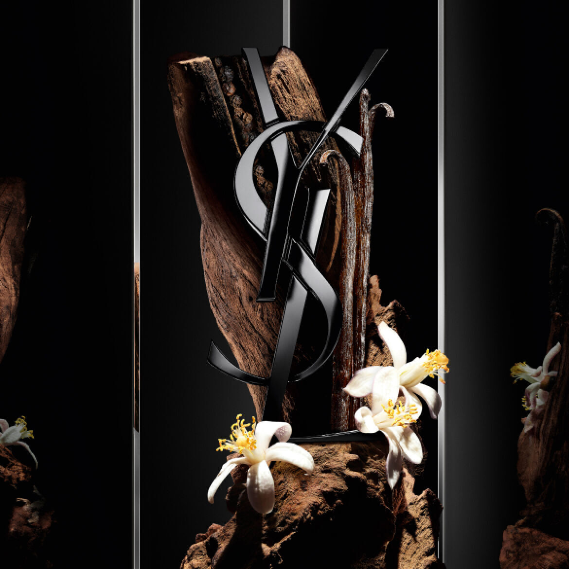 A striking display featuring an artistic arrangement of dark wood and white flowers, with a prominent glossy black YSL logo integrated into the composition. The background is sleek and reflective, enhancing the elegance of the design.