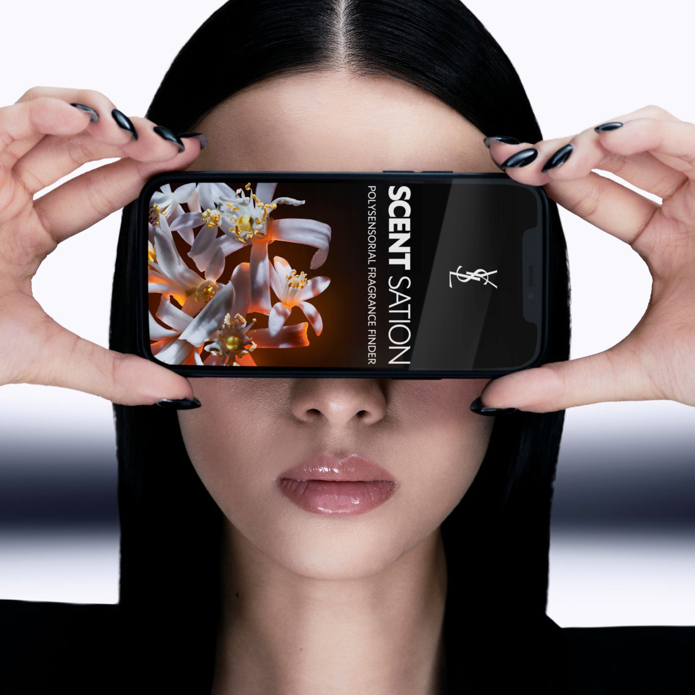 Person holding a smartphone covering their eyes, displaying "SCENT SATION POLYSENSORIAL FRAGRANCE FINDER" and white flowers on screen.