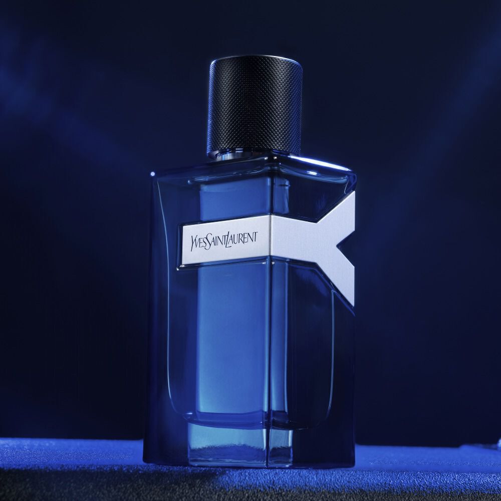 A bottle of Yves Saint Laurent perfume with a sleek blue design and a distinctive logo, illuminated against a dark background.