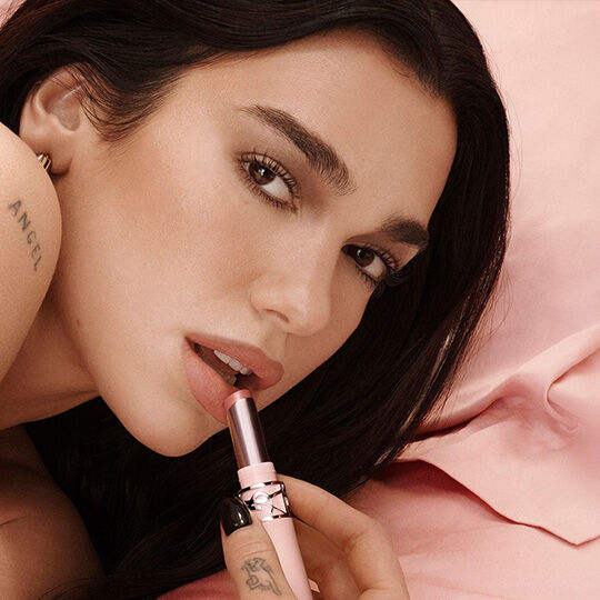 Dua Lipa applying YSL lipstick on a powdery pink background.​