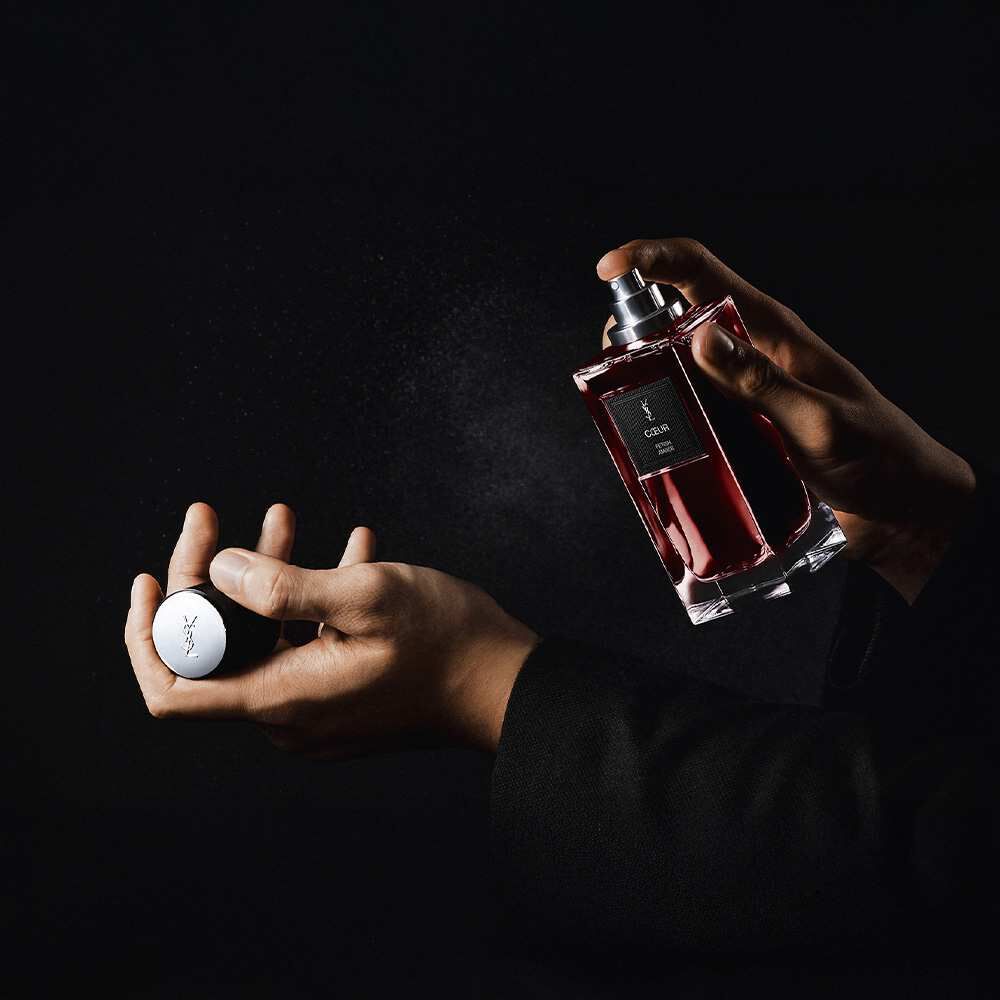 A person sprays YSL "Coeur Battant" perfume onto their wrist.