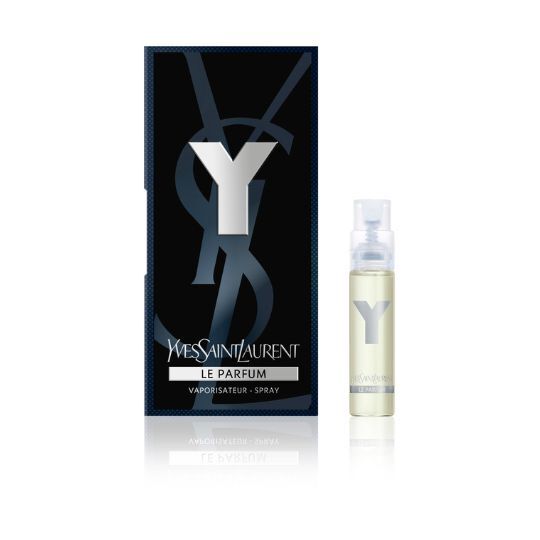 A small bottle of Yves Saint Laurent's "Y Le Parfum" fragrance, displayed in front of its black and silver packaging. The bottle is clear, showcasing the light yellow liquid inside.