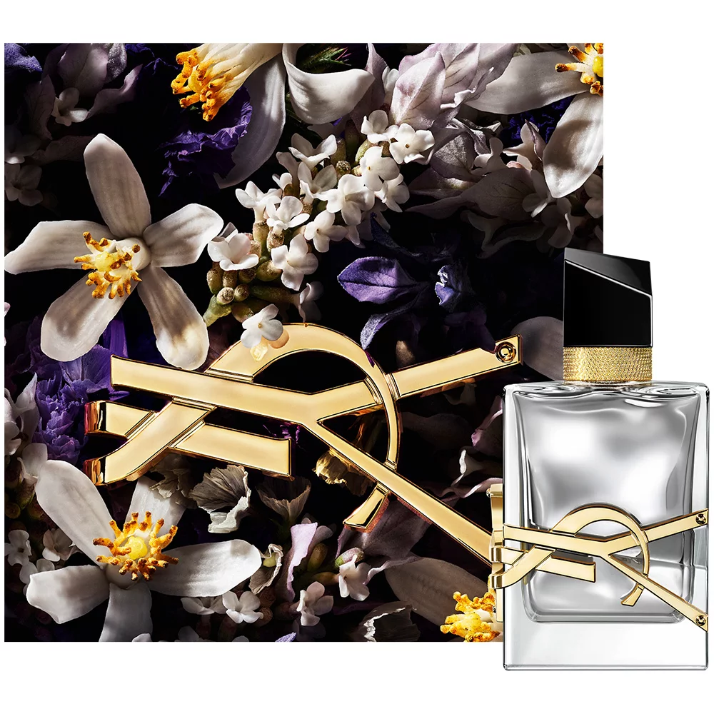 A bottle of perfume featuring a sleek, modern design with a gold logo, placed in front of a floral background with a mix of purple and white flowers.