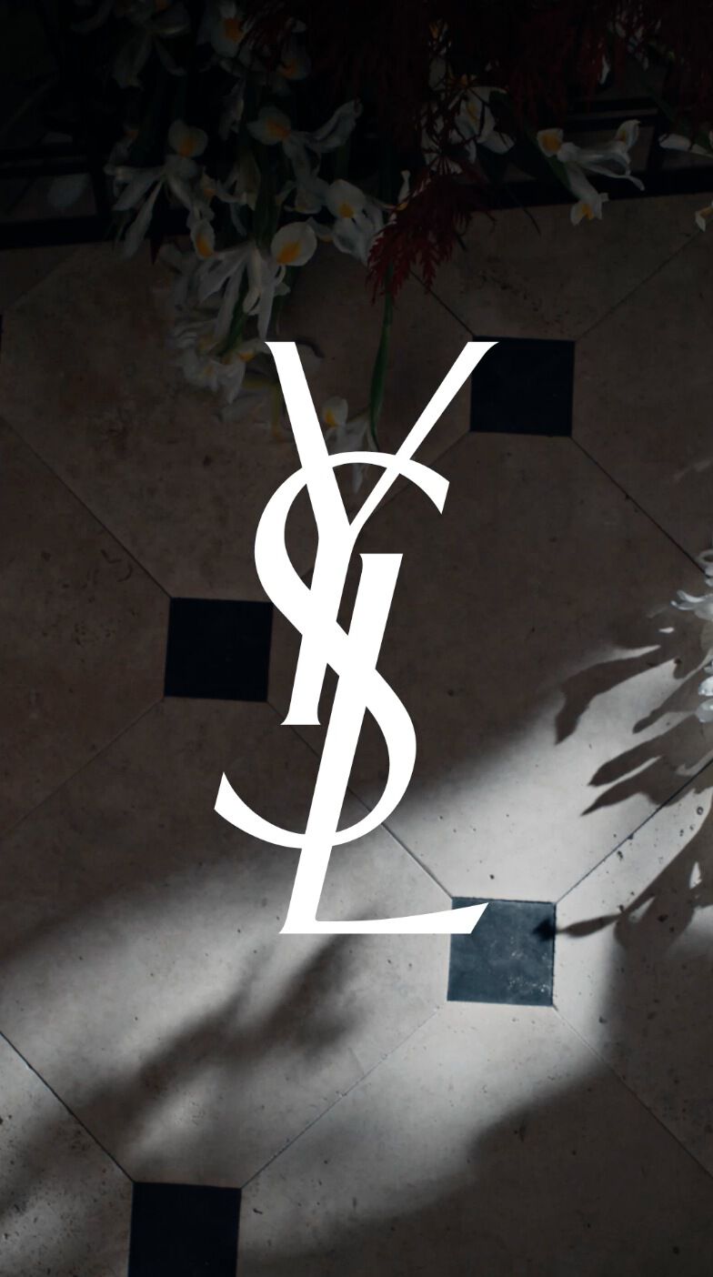 A stylish floor with a geometric pattern of black and white tiles, featuring the iconic YSL logo in the center, surrounded by delicate flowers and dramatic shadows.