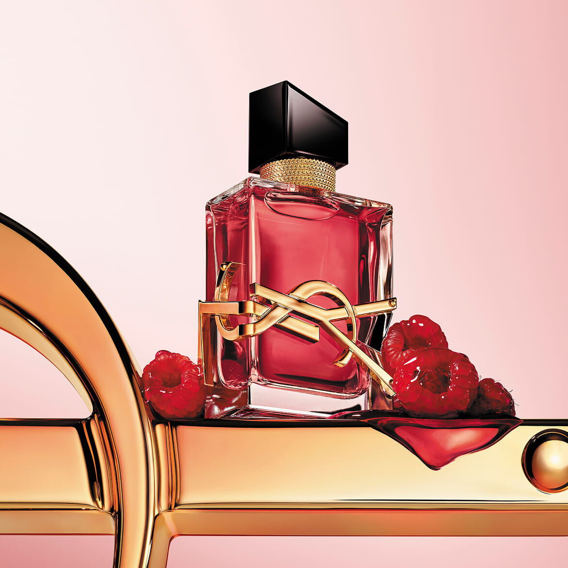 The scarlet YSL LIBRE Berry Crush bottle, with its vibrant essence, rests upon a majestic golden logo, surrounded by succulent raspberries, promising an audacious and irresistible signature.​