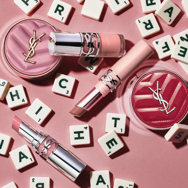 YSL makeup products and letter tiles on a pink background.
