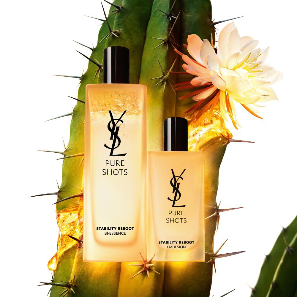 Two YSL Pure Shots skincare products, a bi-essence and an emulsion, set against a cactus with a blooming white flower.