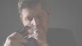 A man in a dark top holds a perfume bottle to his nose, deeply inhaling its scent.