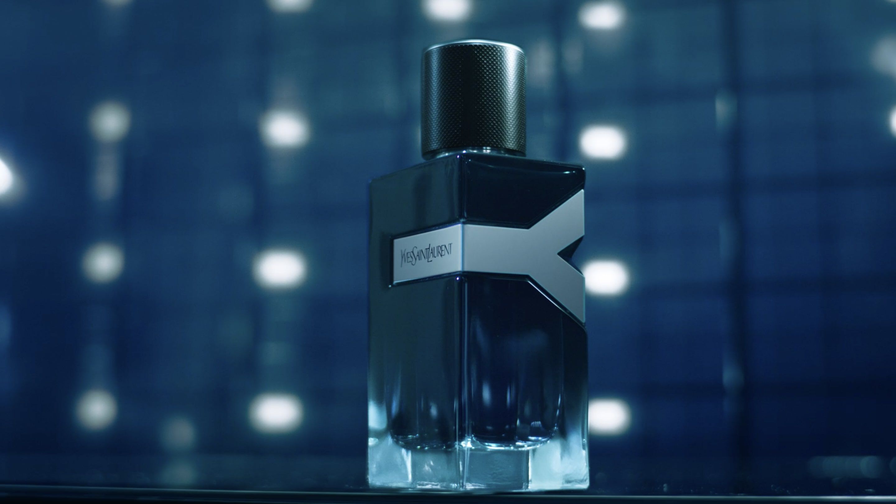 A stylish bottle of cologne with a sleek design, set against a blurred blue background with soft, glowing lights.