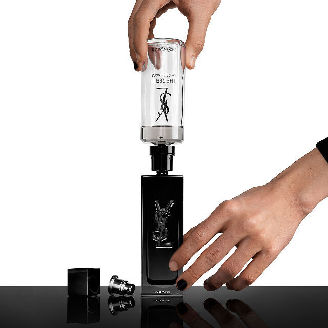 A person's hands refilling a black Yves Saint Laurent (YSL) perfume bottle with a clear refill cartridge that says "THE REFILL LA RECHARGE."