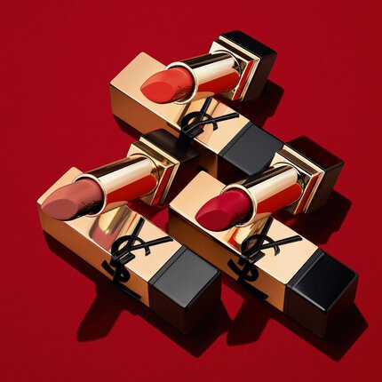 Three luxurious lipsticks with gold packaging lying on a vibrant red background, showcasing shades of red and nude.
