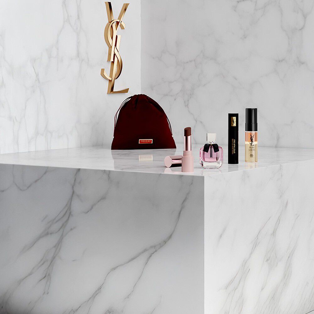 Pink YSL Beauty pouch with lipstick, eyeliner, perfume, and mascara on a marble shelf.