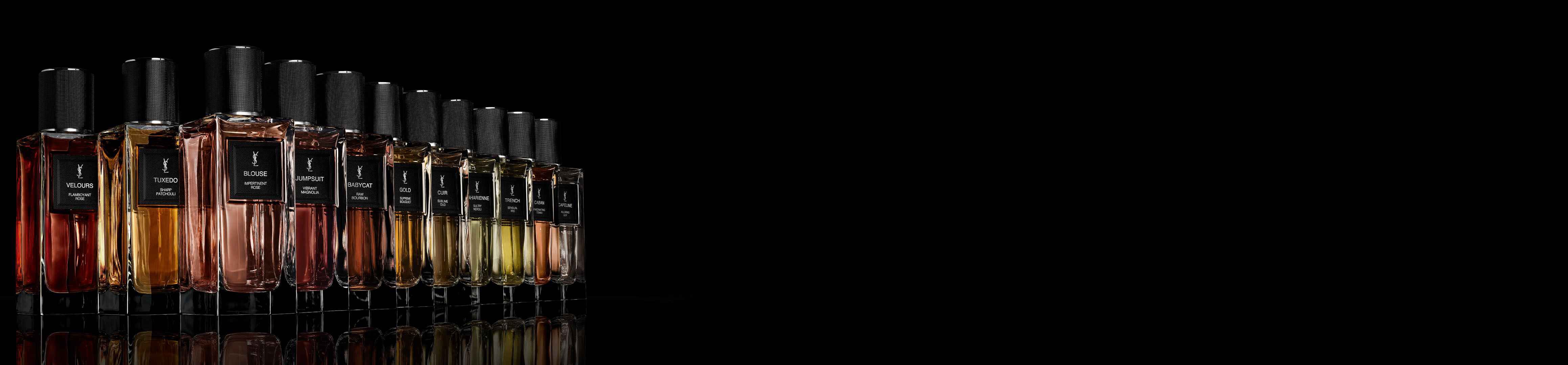 A row of Yves Saint Laurent perfume bottles with various liquid colors and black textured caps, reflecting on a dark surface against a black background.