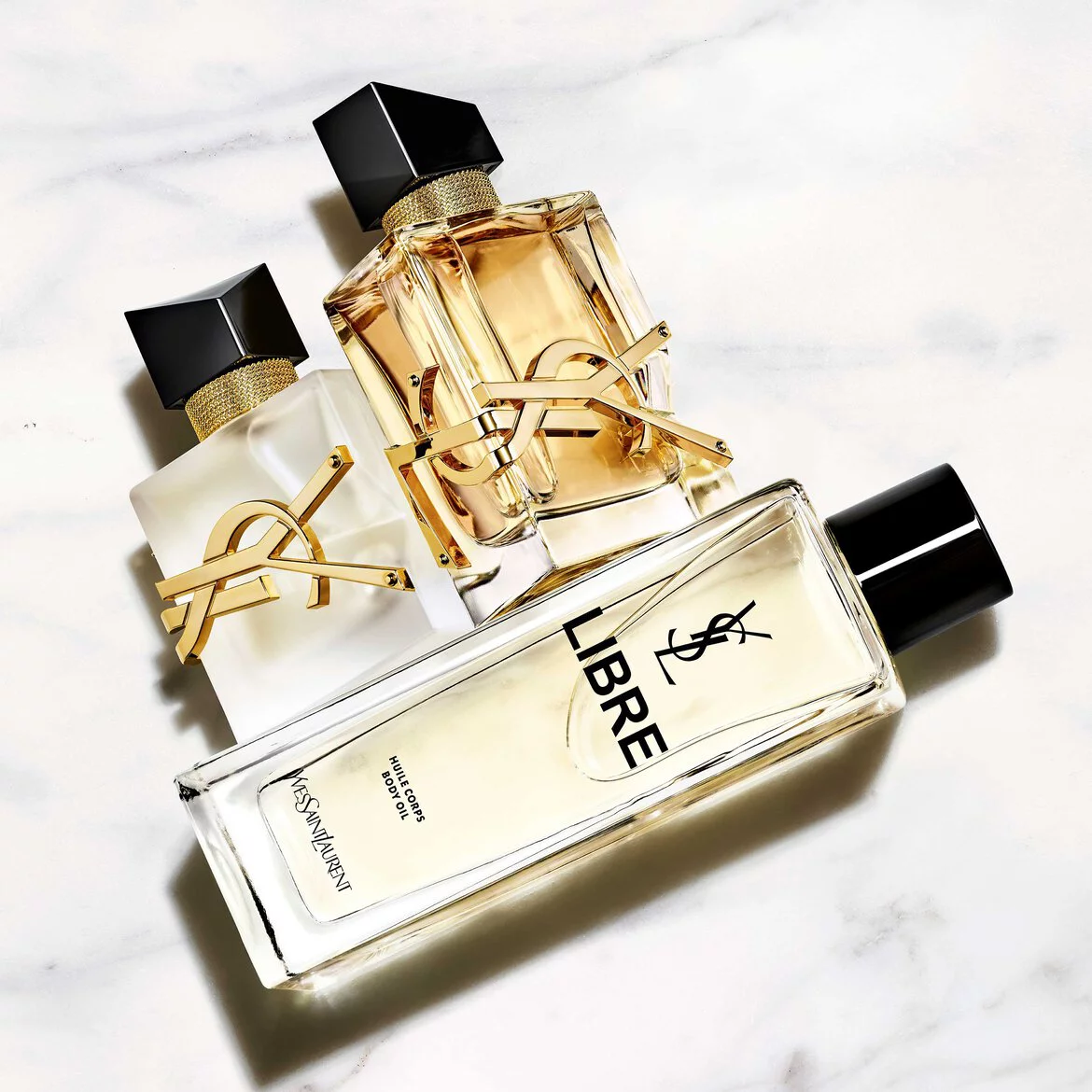 An arrangement of four Yves Saint Laurent perfumes and body products on a marble surface, showcasing elegant packaging with the brand's logo.