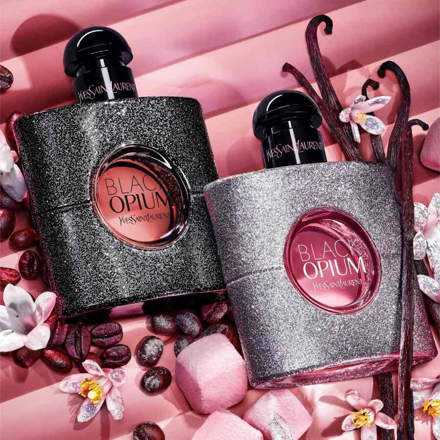 Two YSL Black Opium bottles on pink background with flowers and coffee beans.