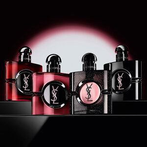 Black Opium perfume bottle surrounded by vanilla, coffee beans, jasmine, and cherries on a red background