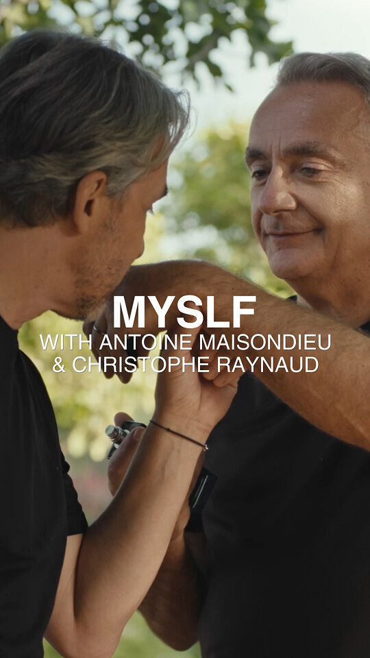 Two men in black t-shirts interact outdoors, with one holding the other's arm and a small object. The image is overlaid with the text "MYSLF WITH ANTOINE MAISONDIEU & CHRISTOPHE RAYNAUD" against a blurry green foliage background.