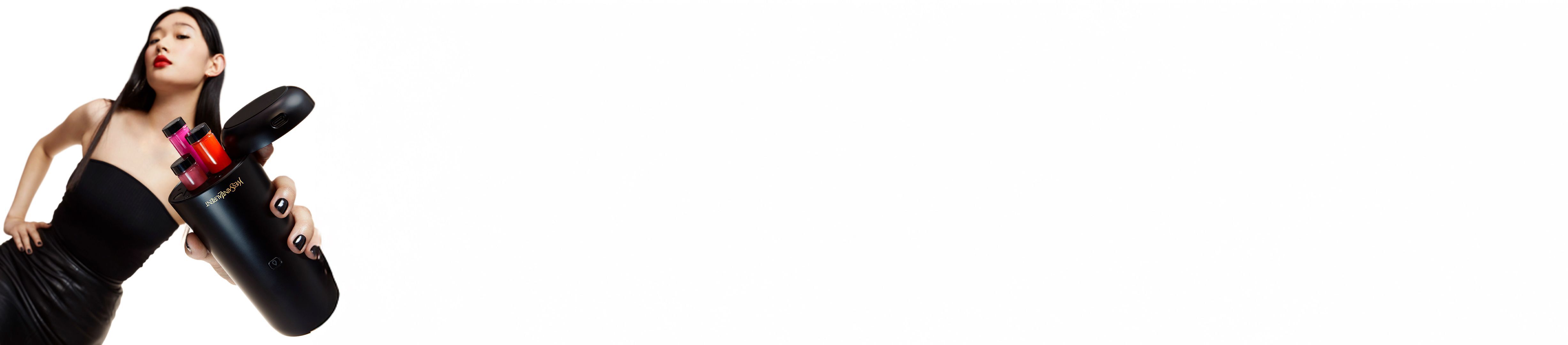 A woman with red lipstick holding a black Yves Saint Laurent beauty device with colorful cosmetic inserts.