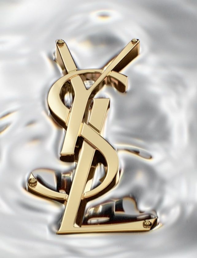 A gold YSL logo resting on a textured, reflective water surface.