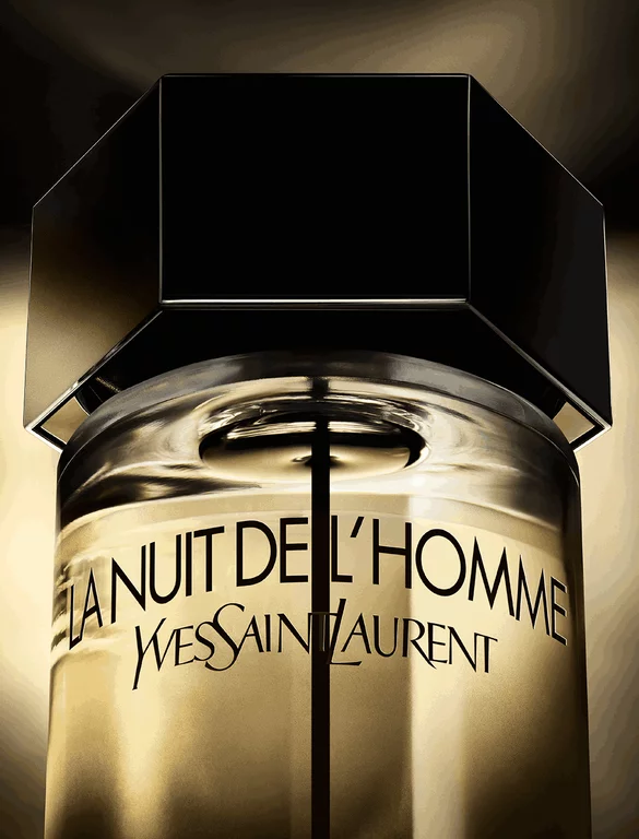 A dark bottle of Yves Saint Laurent's "La Nuit de L'Homme" fragrance, positioned in soft light with a shadowed background, highlighting its sleek design.