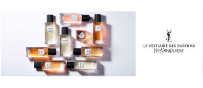 A display of various Yves Saint Laurent perfume bottles arranged aesthetically, featuring a mix of colors and shapes, with the brand name and collection title "Le Vestiaire des Parfums" prominently in the center.