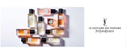A display of various Yves Saint Laurent perfume bottles arranged aesthetically, featuring a mix of colors and shapes, with the brand name and collection title "Le Vestiaire des Parfums" prominently in the center.
