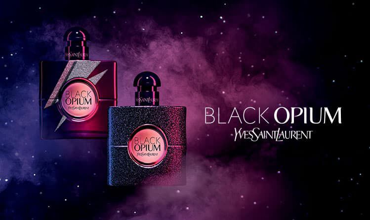 Two stylish perfume bottles of "Black Opium" are displayed against a cosmic background of purple and black smoke, highlighting their sleek and modern design.
