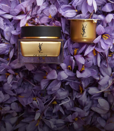 A luxurious skincare cream and a small jar placed on a bed of vibrant purple flower petals, featuring YSL branding.