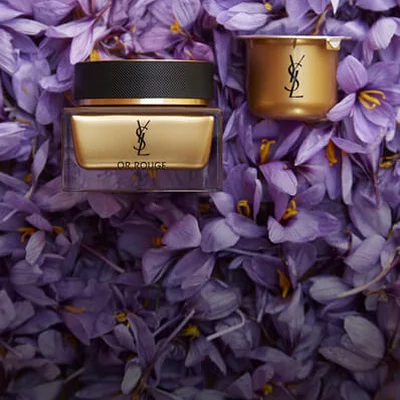 A luxurious skincare cream and a small jar placed on a bed of vibrant purple flower petals, featuring YSL branding.